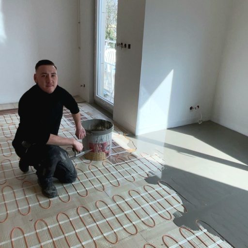 Artisan posant un ragréage sur un sol équipé d’un chauffage au sol électrique, en pleine rénovation d’intérieur